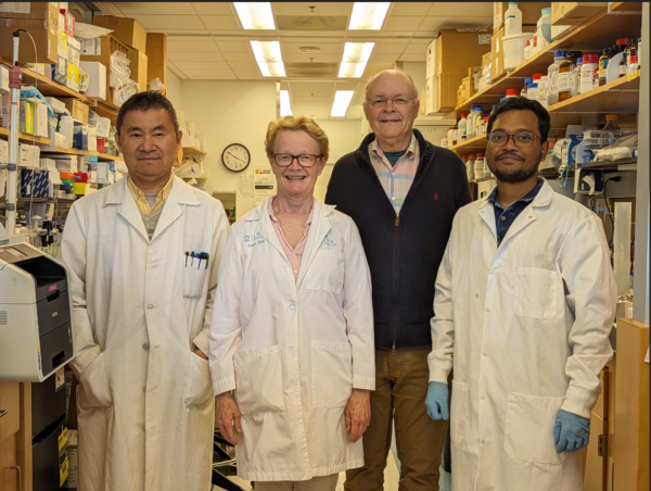 four members of the Charlie Carter Lab in May 2024 standing in the lab with lab coats on smiling with Dr. Carter