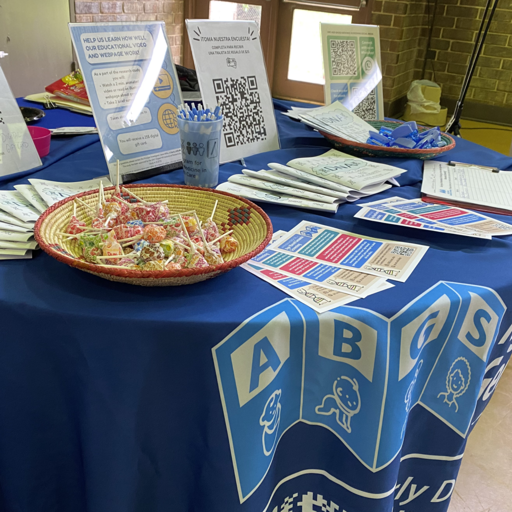 Table displaying items from the Age-Based Genomic Screening project including informational handbills, educational comics, flyers, pens, and candy for those who stop by the table.