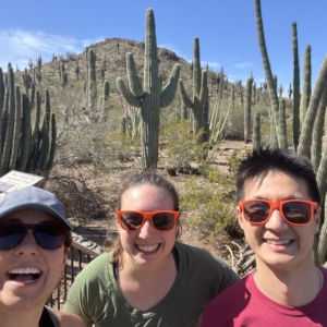 three people standing in front or saguaro cacti in a desert